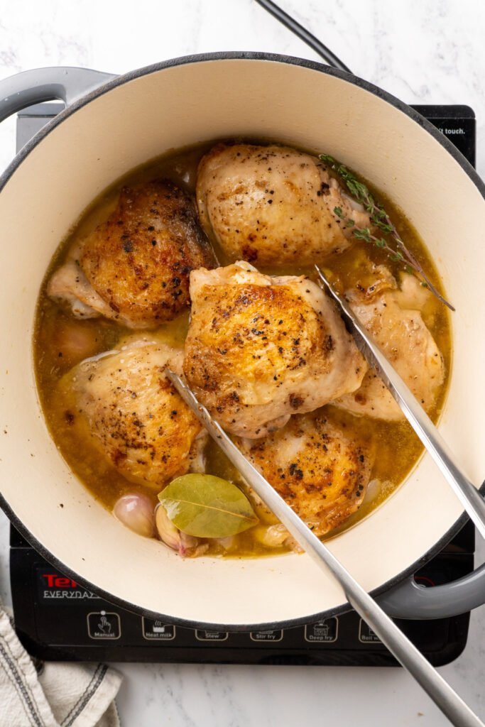chicken thighs in a Dutch oven with a tong